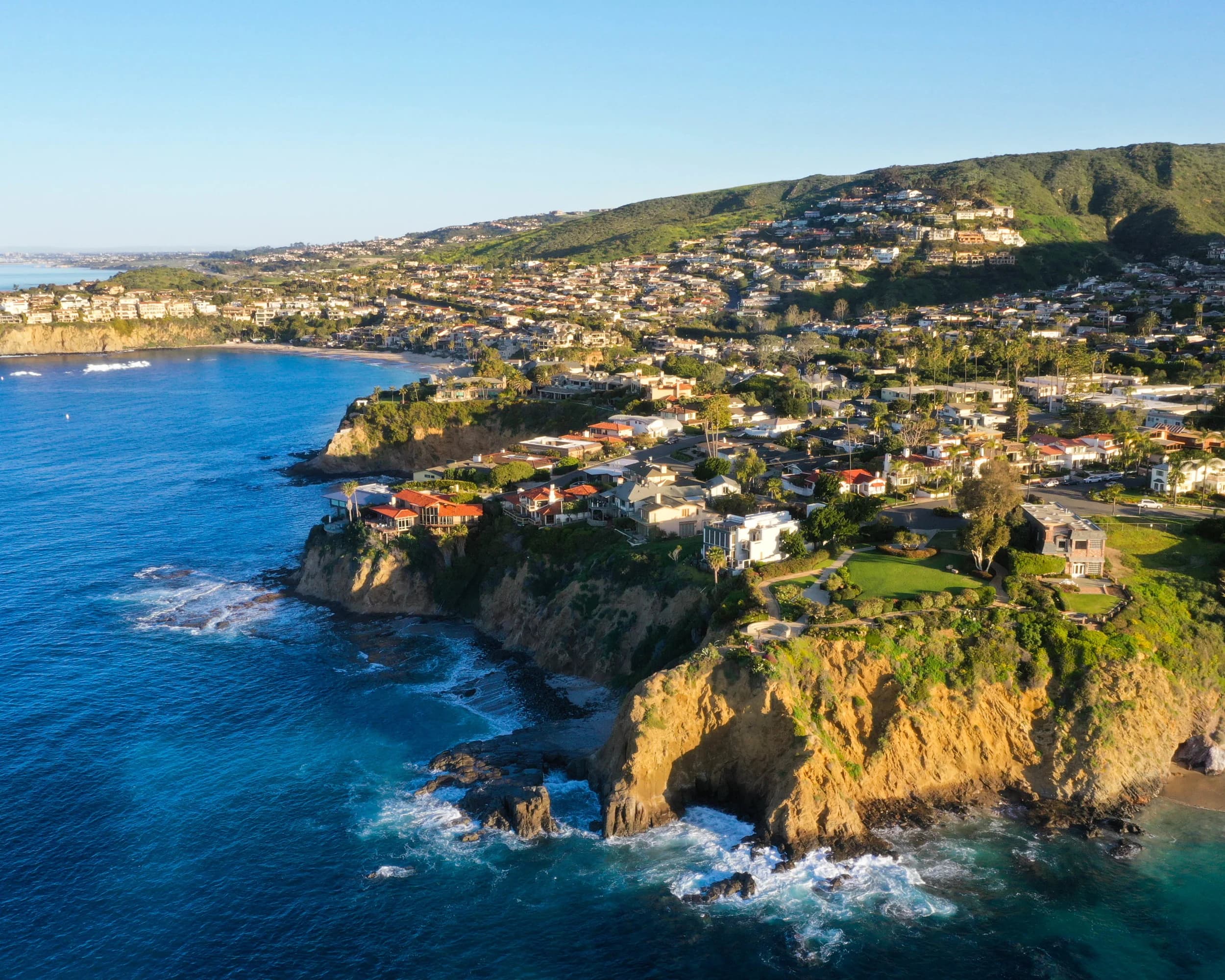 Aerial view of a calm coastal cove with cliffside homes and turquoise water